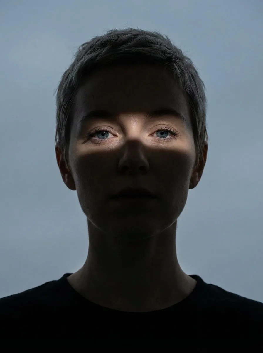 Stable Diffusion prompt: Close-up portrait of a woman (Same face as reference image)looking directly at the camera. Her face and neck are mostly obscured by deep shadow. A single