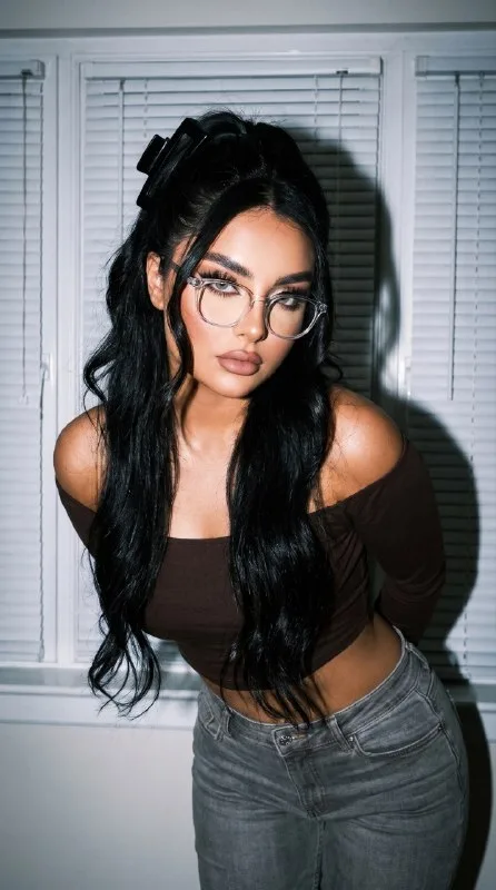 A tanned young woman in a frontal, slightly leaning-forward pose, S-curve, shoulders back, hands behind her