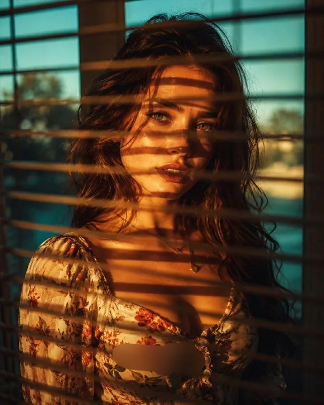Cinematic portrait of [SUBJECT, replace with photo], standing behind window blinds/venetian shutters, warm golden-hour sunlight streaming
