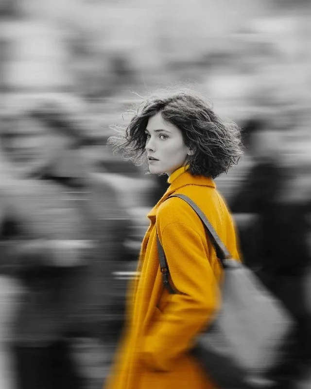 A cinematic street portrait of a beautiful young woman wearing a vibrant mustard-yellow coat while walking