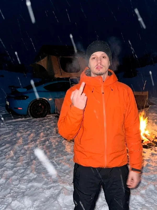 Deep in snow-covered mountains, a raw, nighttime alpine camping scene unfolds during an active snowfall. Partially