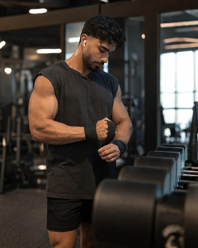 Ultra-realistic fitness editorial photography, muscular male athlete standing beside a dumbbell rack tightening his lifting wrist