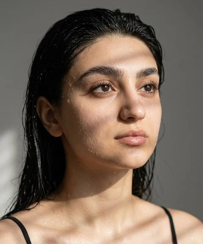 Ultra-realistic portrait of a young woman with wet hair, looking slightly upward to the right. Soft