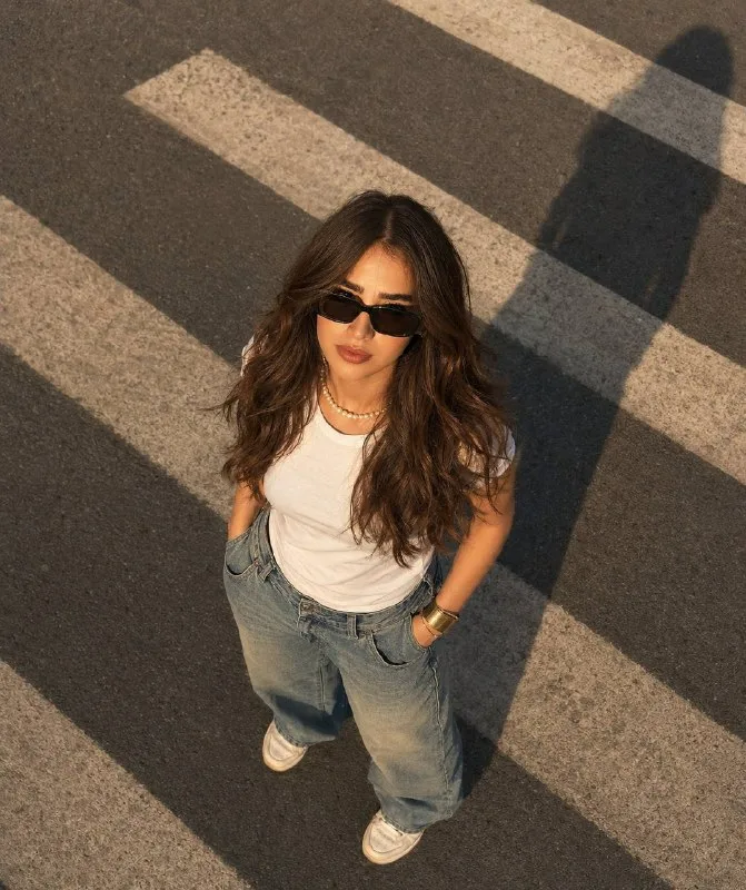 A bird’s-eye view of a girl standing on a pedestrian crosswalk. The warm light of the